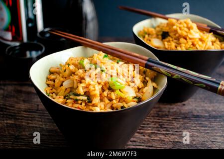 Riso fritto con bacchette appoggiate sulle ciotole: Due ciotole di bokkeumbap kimchi coreano a base di cavolo fermentato Foto Stock