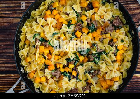 Pasta cremosa di zucca arrosto con salsiccia e spinaci in una padella: Padella piena di cibi dolci fatti con zucca invernale in salsa di panna Foto Stock