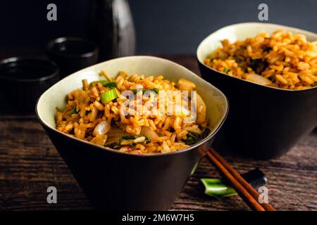 Riso fritto con bacchette accanto alle ciotole: Due ciotole di bokkeumbap kimchi coreano a base di cavolo fermentato Foto Stock