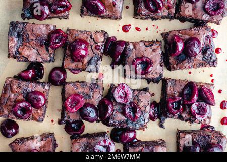 Brownie al cioccolato arrosto Closeup visto dall'alto: Brownie a fette condite con ciliegie tostate su carta pergamena marrone Foto Stock