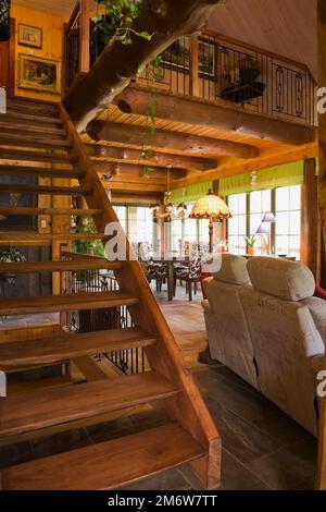 Scale in legno macchiate che conducono al piano superiore e sul retro del divano grigio nel soggiorno all'interno della casa in legno. Foto Stock