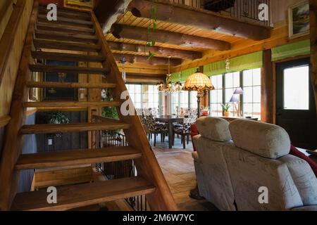 Scale in legno macchiate che conducono al piano superiore e sul retro del divano grigio nel soggiorno all'interno della casa in legno. Foto Stock