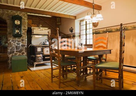 Tavolo in legno antico e sedie con schienale alto, piano cottura modello Sweet Heart anni '1850 realizzato a mano dalla stufa Elmira lavora in cucina all'interno di una casa di legno. Foto Stock