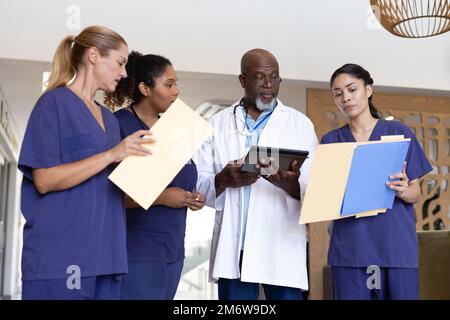 Gruppo eterogeneo di operatori sanitari con tablet e documenti che discutono in corridoio ospedaliero Foto Stock