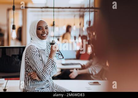 Protarit di una donna musulmana nera (afro-americana) in piedi in un moderno ufficio d'affari mentre indossa un hijab. Foto Stock