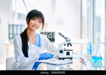 Sorridente scienziata asiatica in posa in moderno laboratorio di ricerca medica Foto Stock