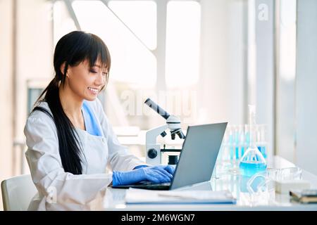 Felice scienziato femminile che lavora al suo computer in moderno laboratorio di ricerca medica Foto Stock