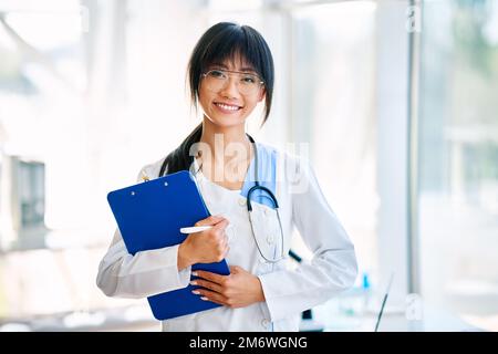Sorridente medico sicuro femmina che tiene la clipboard in posa in ospedale Foto Stock
