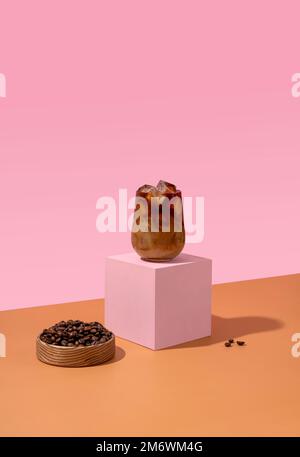 Gelato in un bicchiere alto con panna versata e chicchi di caffè su sfondo rosa. Foto Stock
