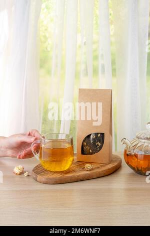 Branding del tè biologico e mockup dell'imballaggio. Tè verde gelsomino in teiera di vetro sul tavolo. Il tè caldo è nelle tazze di vetro. Teiera e. Foto Stock