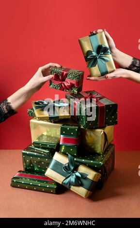 Le mani di una donna arrivano per un dono. Montagne di regali. Vendite per il nuovo anno. Giftbox natalizi con nastro rosso e verde acqua di mare. Foto Stock