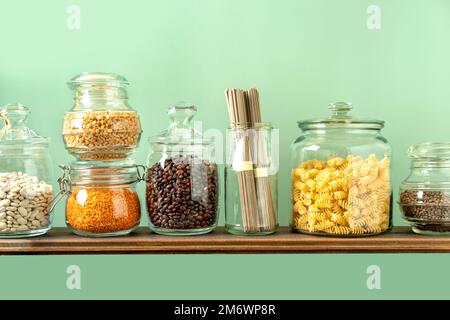 Legumi diversi in vasetti di vetro: Ceci, pasta, fagioli, piselli, lenticchie su fondo verde. Nessun deposito di rifiuti, senza plastica. Foto Stock