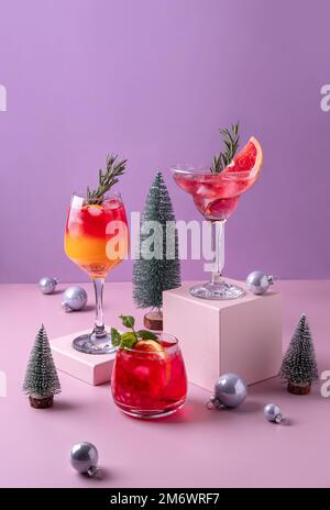 Cocktail di agrumi festosi sui podi. Assortimento di bevande fresche di Natale. Cocktail di sangria rosa e rossa, melograno jingle a Foto Stock