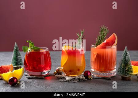 Tre cocktail festosi con vari agrumi. Assortimento di bevande alcoliche di Natale. Cocktail di sangria rosa e rossa, melograno Foto Stock