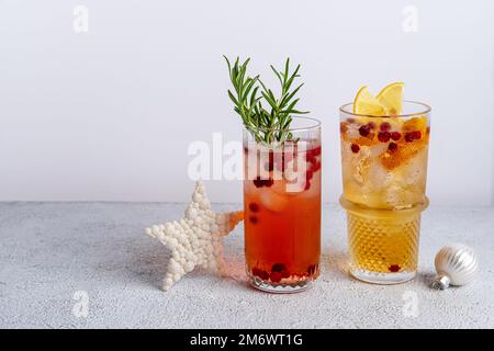 Due cocktail di Natale colorati in bicchieri su un tavolo bianco. Assortimento di bevande fresche per le vacanze. Cocktail di sangria rossa, PU arancione Foto Stock