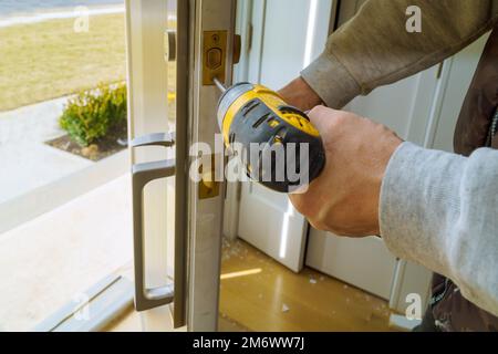 Il lavoratore che installa la serratura in una nuova casa con l'ausilio di un cacciavite Foto Stock