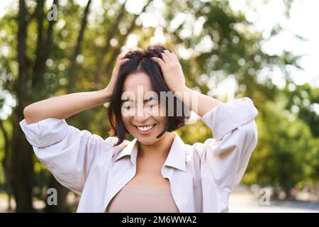 Concetto di persone ed emozioni. Felice donna asiatica ridendo e sorridendo, in posa il giorno d'estate nel parco Foto Stock