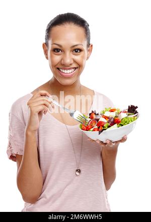 Fare la scelta sana. Ritratto di una giovane donna attraente che mangia una ciotola di insalata isolato su bianco. Foto Stock