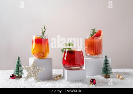Cocktail di agrumi festosi sui podi. Assortimento di bevande fresche di Natale. Cocktail di sangria rosa e rossa, melograno jingle a Foto Stock