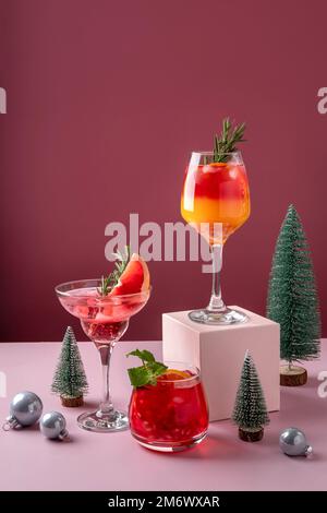 Cocktail di agrumi festosi sui podi. Assortimento di bevande fresche di Natale. Cocktail di sangria rosa e rossa, melograno jingle a Foto Stock
