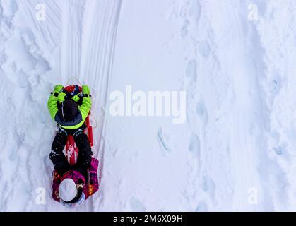 Foto aerea di due bambini in una slitta che scende su una collina innevata. Foto Stock