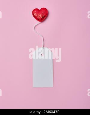 Cartoncino bianco vuoto su corda bianca, sfondo rosa Foto Stock