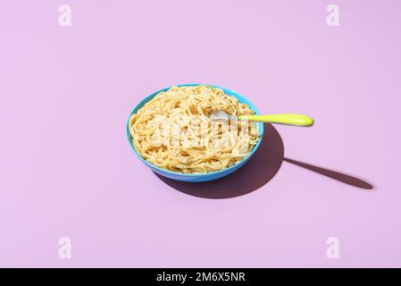 Classico piatto italiano, spaghetti con parmigiano e pepe nero, minimalista su un tavolo viola. Pasta cacio e pepe in luce brillante su un vivace c Foto Stock