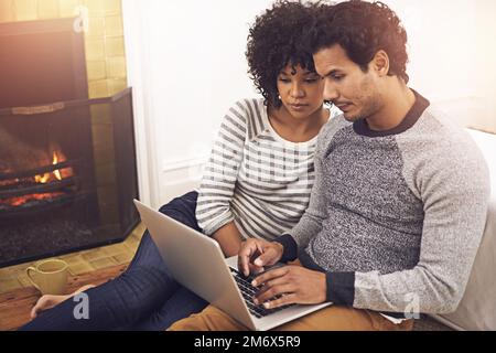 Godendo la loro notte di coppia dentro. una coppia che usa il proprio computer portatile mentre si siede accanto al caminetto a casa. Foto Stock