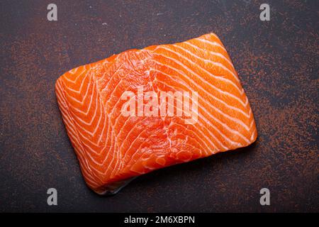 Pezzo di filetto di salmone fresco norvegese crudo su sfondo marrone scuro rustico vista dall'alto, sana alimentazione e dieta Foto Stock