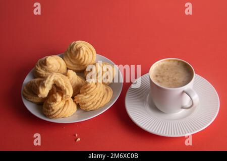 foto di una tazza bianca di caffè e di alcune meringhe dolci su sfondo rosso Foto Stock