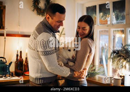 Giovane coppia felice innamorata di carino piccolo cane godendo stagione di vacanza invernale in accogliente casa calda Foto Stock