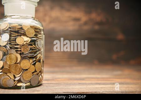 Vaso di vetro riempito di monete d'oro con spazio copia per il testo su sfondo di legno. Foto Stock