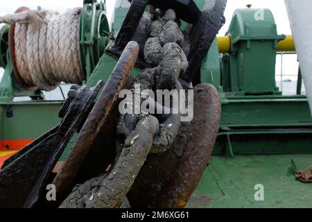 Ancorare la catena dal verricello di ancoraggio sul supporto anteriore. Catena sporca e arrugginita sfondo marittimo Foto Stock