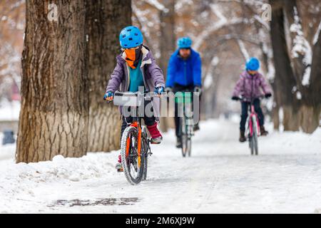 Padre e bambini in bicicletta in inverno. Un uomo con suo figlio e sua figlia cavalcano le biciclette lungo la pista ciclabile nel parco invernale Foto Stock