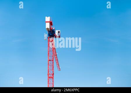 Vista posteriore di una grande gru da cantiere rossa di fronte al cielo azzurro nuvoloso e soleggiato Foto Stock