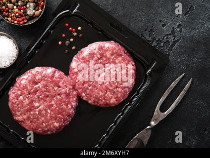 Hamburger biologici di manzo in vassoio vuoto con forchetta e sale e pepe nero. Foto Stock