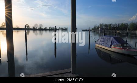 Piccolo motoscafo coperto di telone al molo del Lago di Costanza con i raggi del sole sul lato sinistro del quadro e ragnatela sul terreno Foto Stock