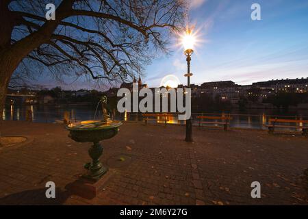 basilea svizzera, la passeggiata sul reno di sera. Sullo sfondo la cattedrale e la ruota panoramica della fiera autunnale. Foto Stock