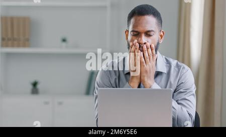 Sottolineato scioccato africano americano etnia sopportato adulto uomo d'ufficio uomo d'affari con computer portatile triste sconvolto frustrato lettura online cattive notizie Foto Stock