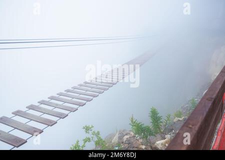 Ponte sospeso turistico in nebbia profonda. Ponte sospeso in corda che svanisce, vista frontale. Foto Stock