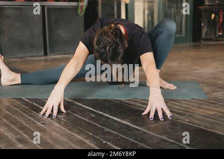 Donna irriconoscibile Yogi nuovo insegnante giovane adulto che fa una posa skandasana con piega in avanti e braccia estese con leggings verdi nella sua pratica di yoga Foto Stock