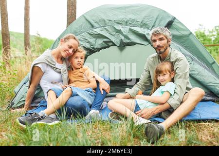I genitori trascorrono del tempo libero con i bambini mentre si siedono fuori dalla tenda del campeggio Foto Stock
