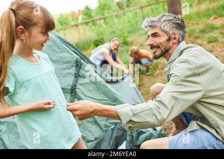 Figlia sorridente aiutando padre nella messa in tenda mentre campeggio nella foresta durante le vacanze estive Foto Stock