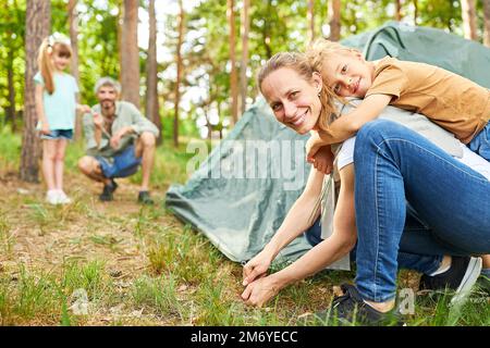 Ritratto di donna felice piggybacking figlio durante la messa in tenda in foresta durante le vacanze estive Foto Stock