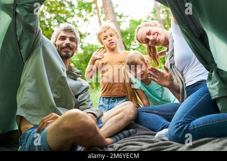 Genitori felici che agitavano le mani mentre si allestiva una tenda con bambini nella foresta durante le vacanze Foto Stock