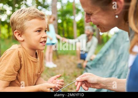 Ragazzo che tiene i pioli della tenda e che parla con la madre mentre campeggio nella foresta durante le vacanze Foto Stock