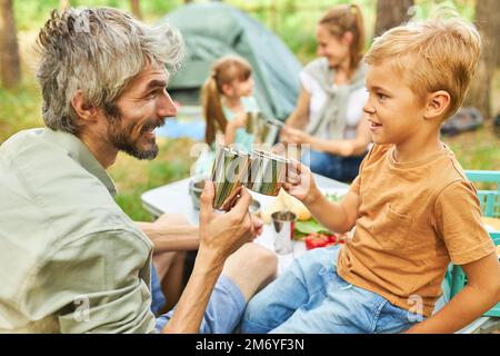 Padre e figlio brinda le tazze mentre campeggio nella foresta durante le vacanze estive Foto Stock