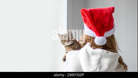 adorabile carino gatto tabby seduto sul davanzale finestra o donna ragazza proprietario shoulder.young pelliccia femmina e ragazza che indossa sulla testa babbo natale cap.hat Foto Stock