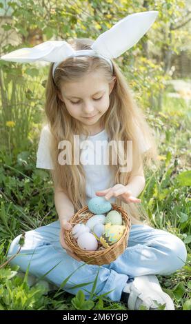 Grazioso fanciullo indossando orecchie di coniglietto il giorno di Pasqua. Ragazza con cesto con uova dipinte. Foto Stock