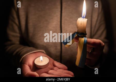 Blackout. Crisi energetica. Concetto di interruzione dell'alimentazione. La ragazza tiene in mano due candele bruciate con un nastro giallo-blu (il simbolo nazionale dell'Ucraina) Foto Stock